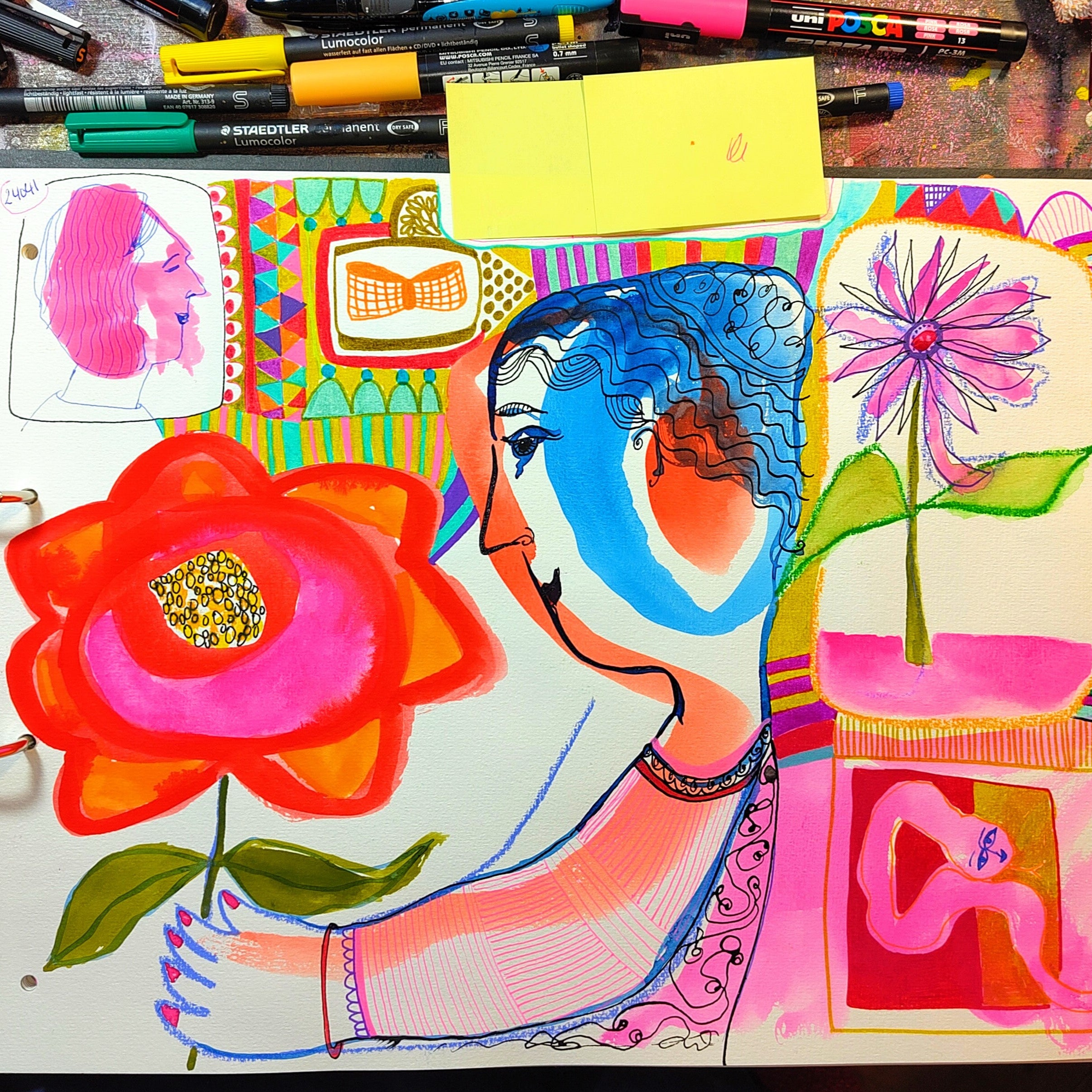 Colorful artwork with abstract figures and flowers on a desk with art supplies.